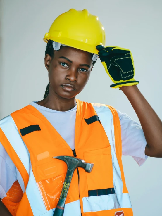 a woman in an orange safety vest holding a hammer, trending on pexels, non binary model, maria borges, hard hat, post graduate