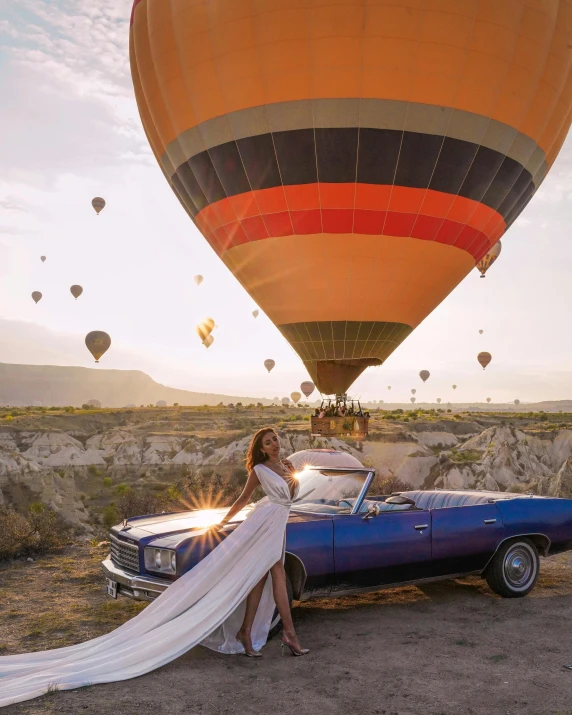 a woman standing next to a car in front of a hot air balloon, a colorized photo, inspired by Hedi Xandt, pexels contest winner, on the runway, high above the ground, taliyah, taking a picture