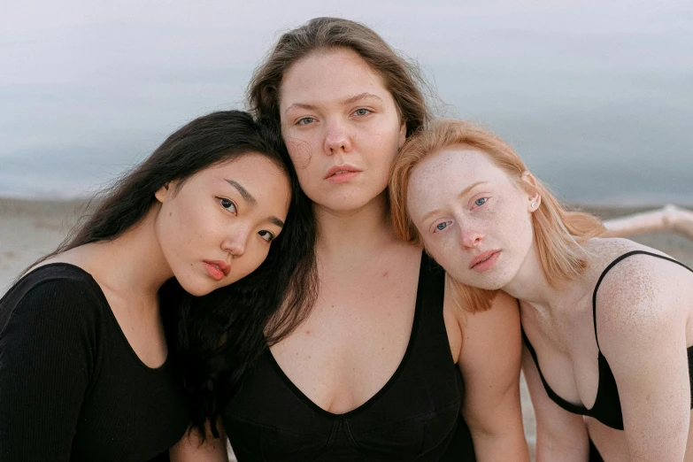 three women sitting next to each other on a beach, unsplash, renaissance, pale round face, she is wearing a black tank top, natural skin tones, with pale skin