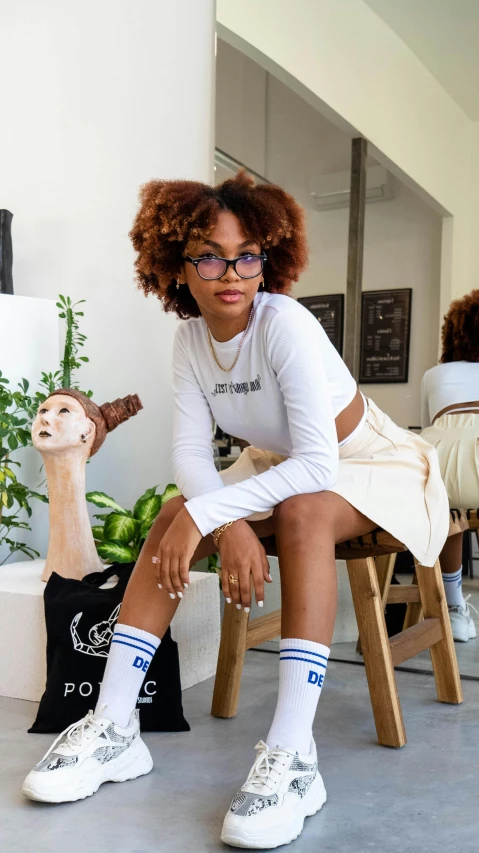 a woman sitting on top of a wooden chair, by Jessie Alexandra Dick, featured on instagram, wearing honey - themed miniskirt, afropunk, on a white table, nerdy appearance