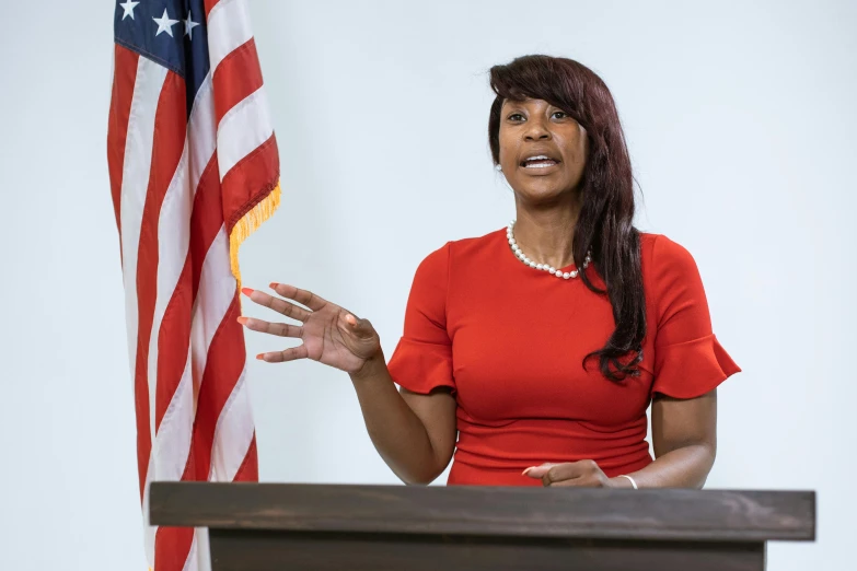 a woman standing at a podium in front of an american flag, vanessa blue, 4k photo”, alabama, 15081959 21121991 01012000 4k