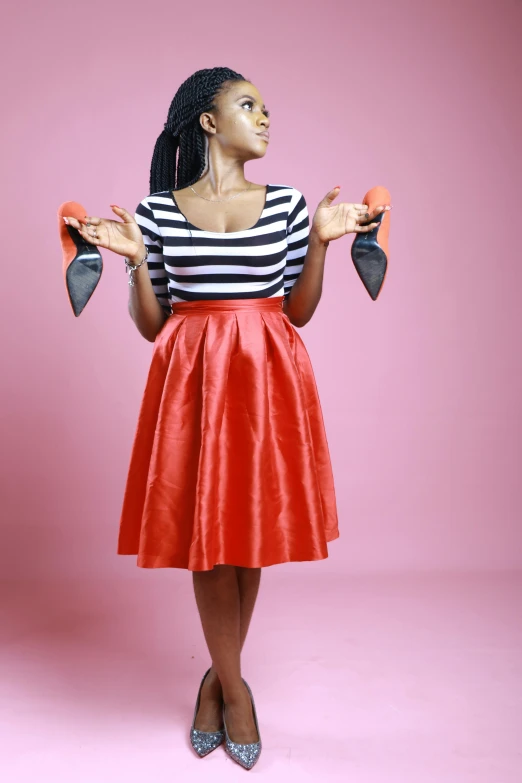 a woman in a red skirt holding a pair of shoes, an album cover, by Chinwe Chukwuogo-Roy, pexels, wearing stripe shirt, studio shoot, holding a bow, 15081959 21121991 01012000 4k