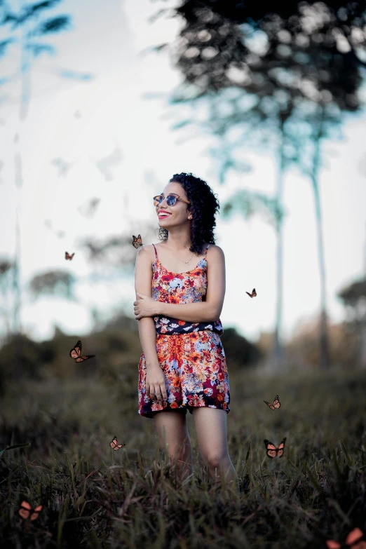 a woman standing in a field with butterflies flying around her, by Lucia Peka, pexels contest winner, girl wearing round glasses, nathalie emmanuel, plethora of colors ; mini dress, low quality photo