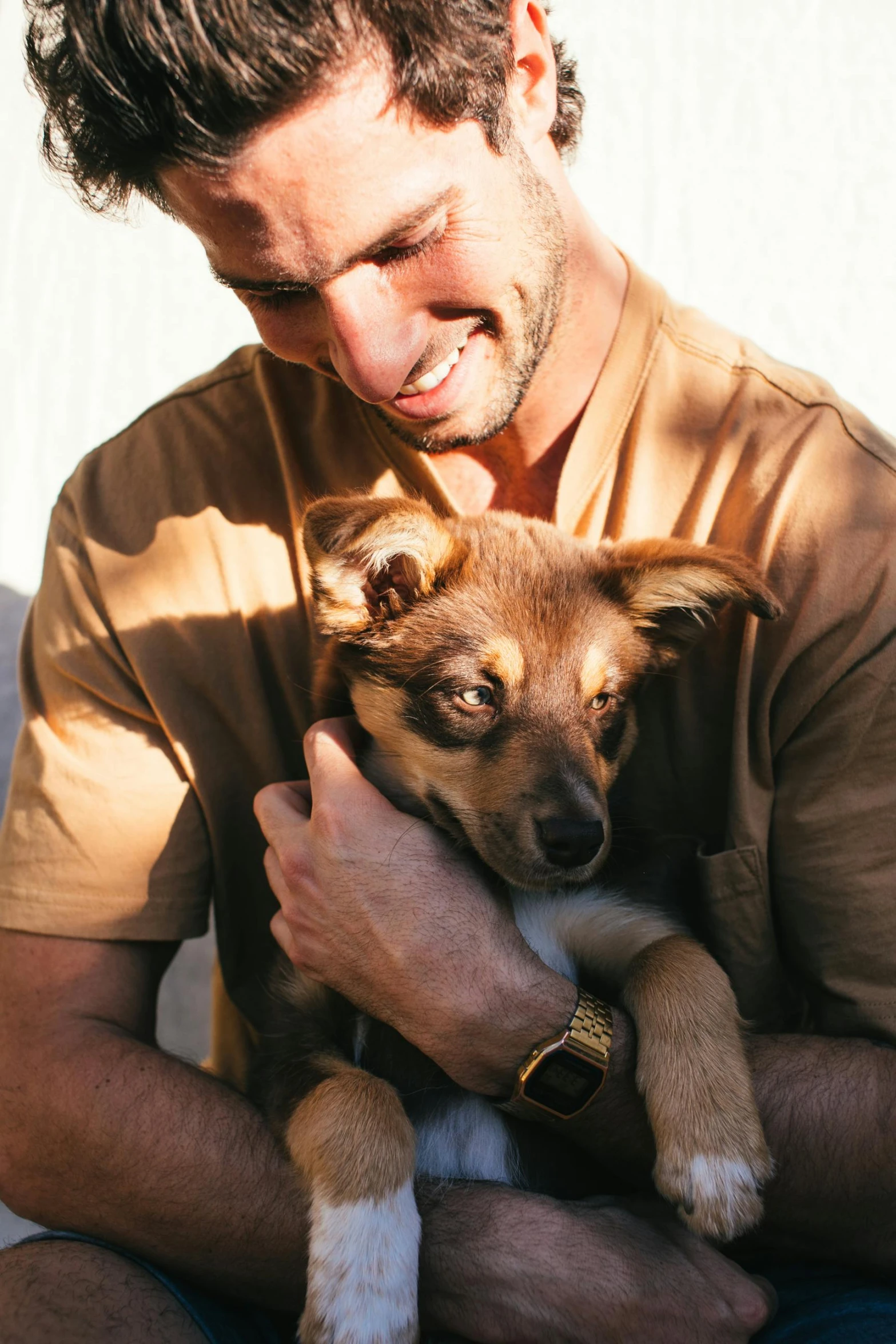 a man sitting on a couch holding a small dog, ruggedly handsome ranger, hugging and cradling, profile image, sunshine