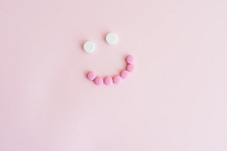 a smiley face made out of pills on a pink background, by Emma Andijewska, minimalism, minimalist photo, emoticon, candy, uploaded
