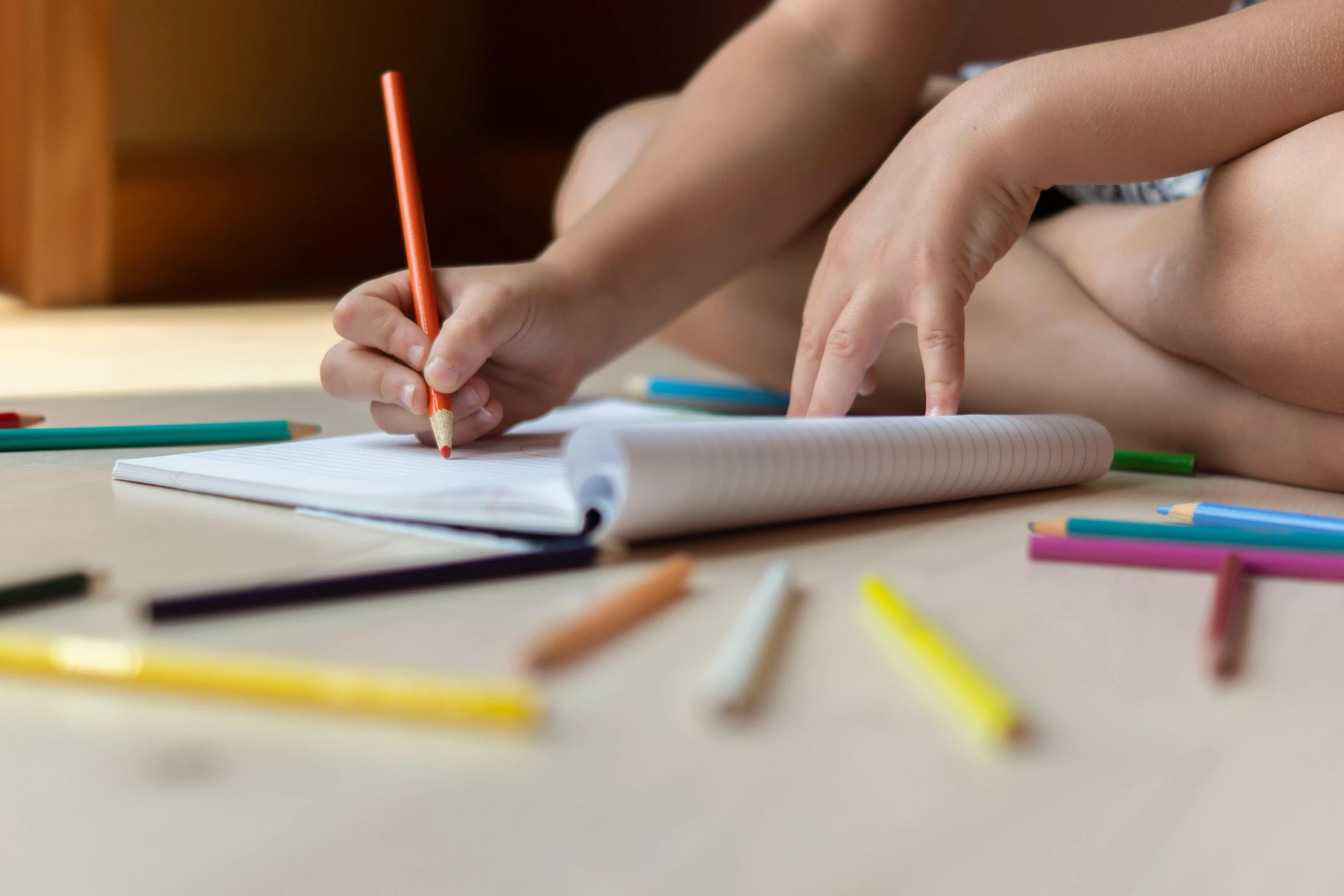 a child sitting on the floor drawing with colored pencils, pexels contest winner, holding notebook, hand on table, thumbnail, multiple stories