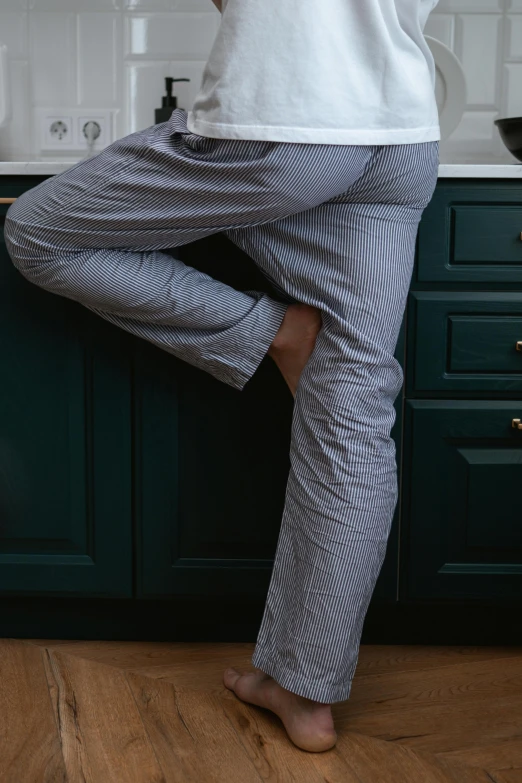a woman standing on one leg in a kitchen, by Alice Mason, unsplash, wearing a baggy pajamas, in gunmetal grey, asleep, masculine pose