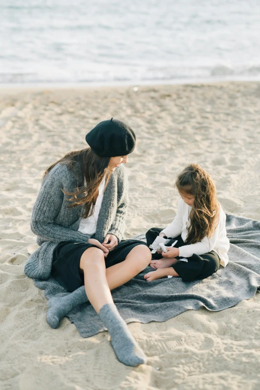 a mother and daughter sitting on a blanket on the beach, by Anita Malfatti, unsplash contest winner, grey clothes, gray shorts and black socks, elegantly dressed, cardigan
