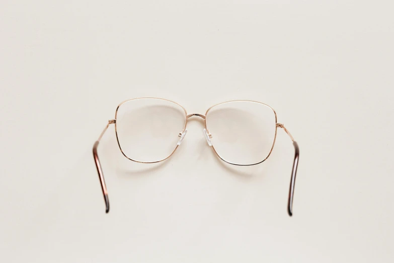 a pair of glasses on a white surface, by Carey Morris, unsplash, clear [bronze] face, light frame, photographed from the back, square glasses