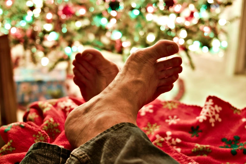 a person laying on a bed in front of a christmas tree, pexels, renaissance, barefeet, focus on his foot, early evening, multicoloured