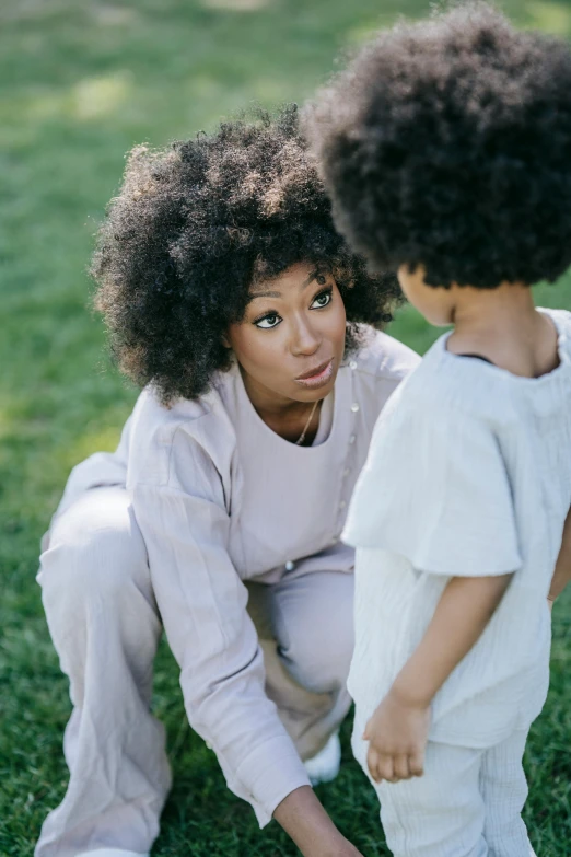 a woman and a child playing with a frisbee, by Lily Delissa Joseph, trending on pexels, renaissance, afro hair, pondering, sitting on one knee on the grass, muted