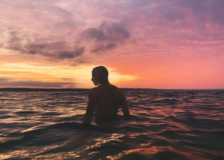 a man sitting in the ocean at sunset, an album cover, by Emma Andijewska, unsplash contest winner, pink skies, manly, thom yorke, swimming across the universe