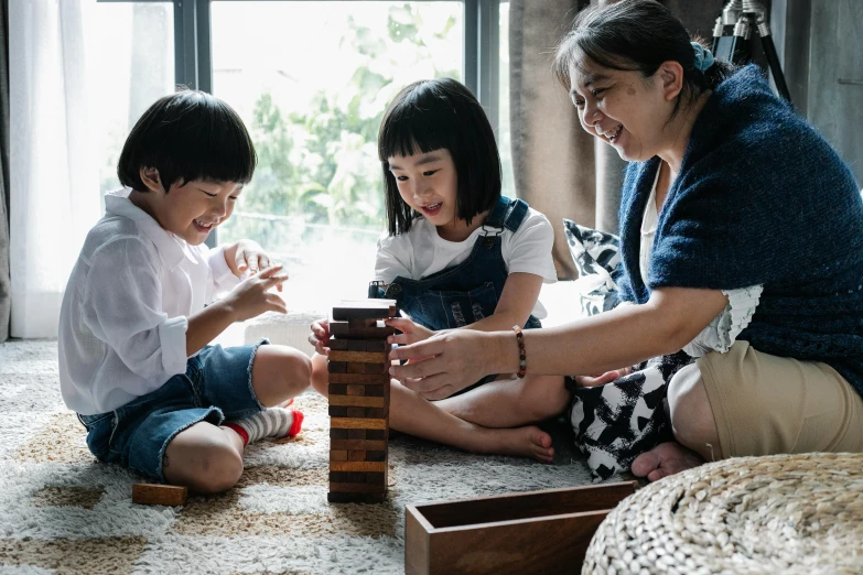 a woman and two children playing with wooden blocks, pexels contest winner, ross tan, casual game, profile image, board games on a table