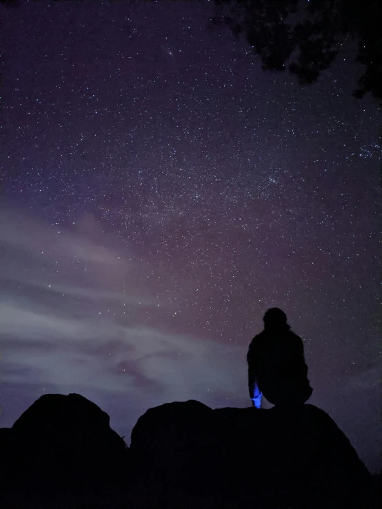 a person sitting on top of a rock under a night sky, facing away from the camera, low quality photograph, trending photo