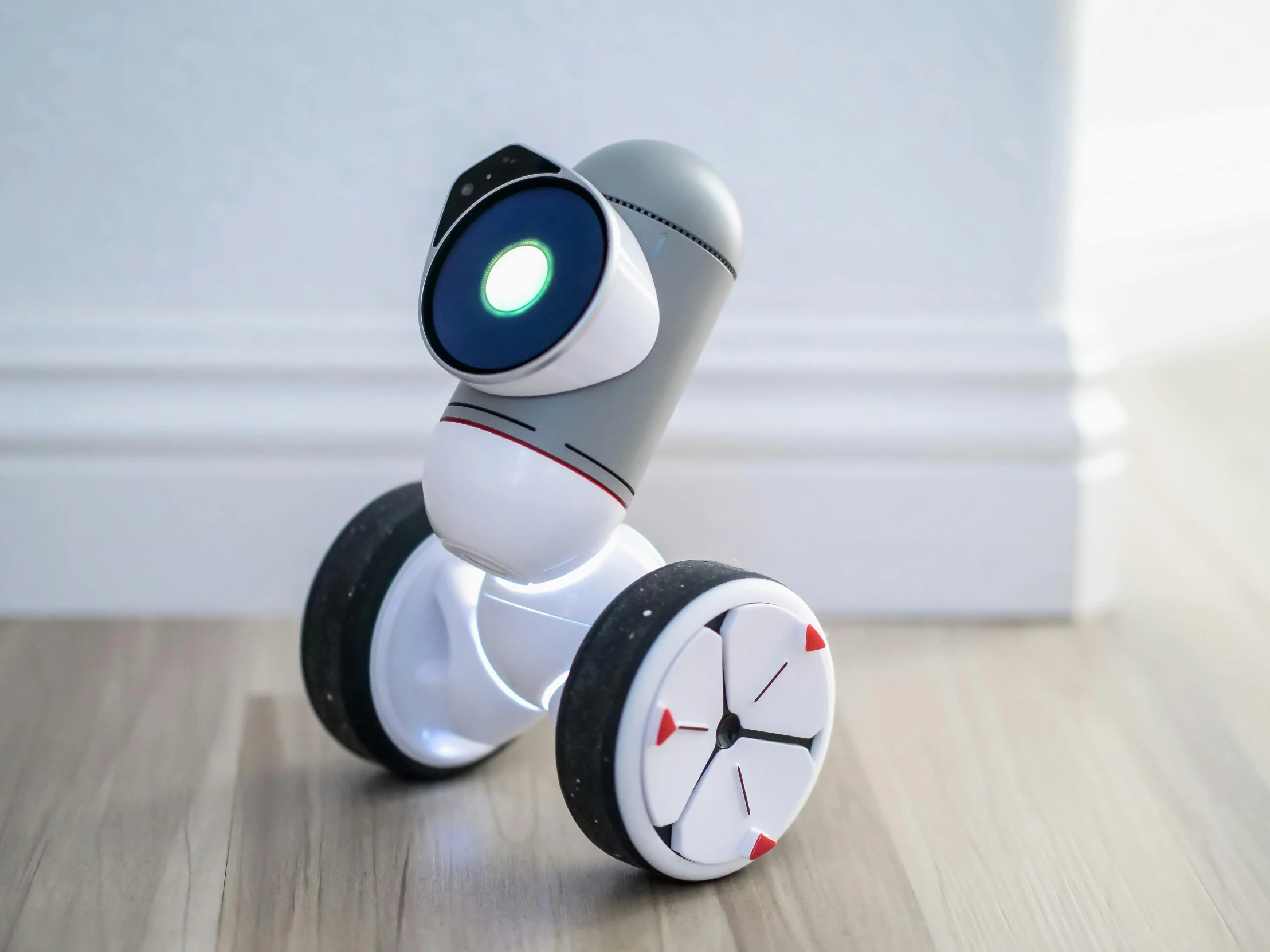 a small robot sitting on top of a wooden floor, ixions wheel, grey, in style of baymax, front angle