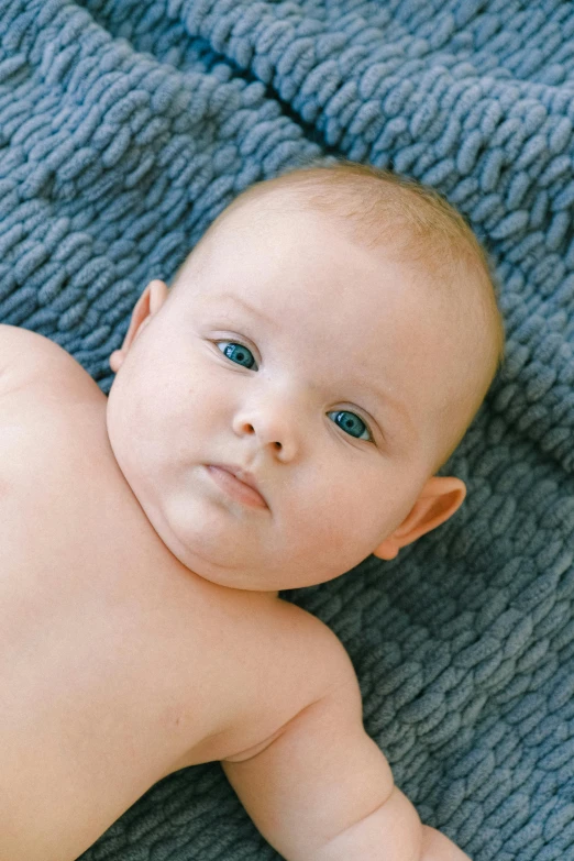 a baby laying on top of a blue blanket, by Nina Hamnett, soft facial features, grey, close - ip shot, lachlan bailey