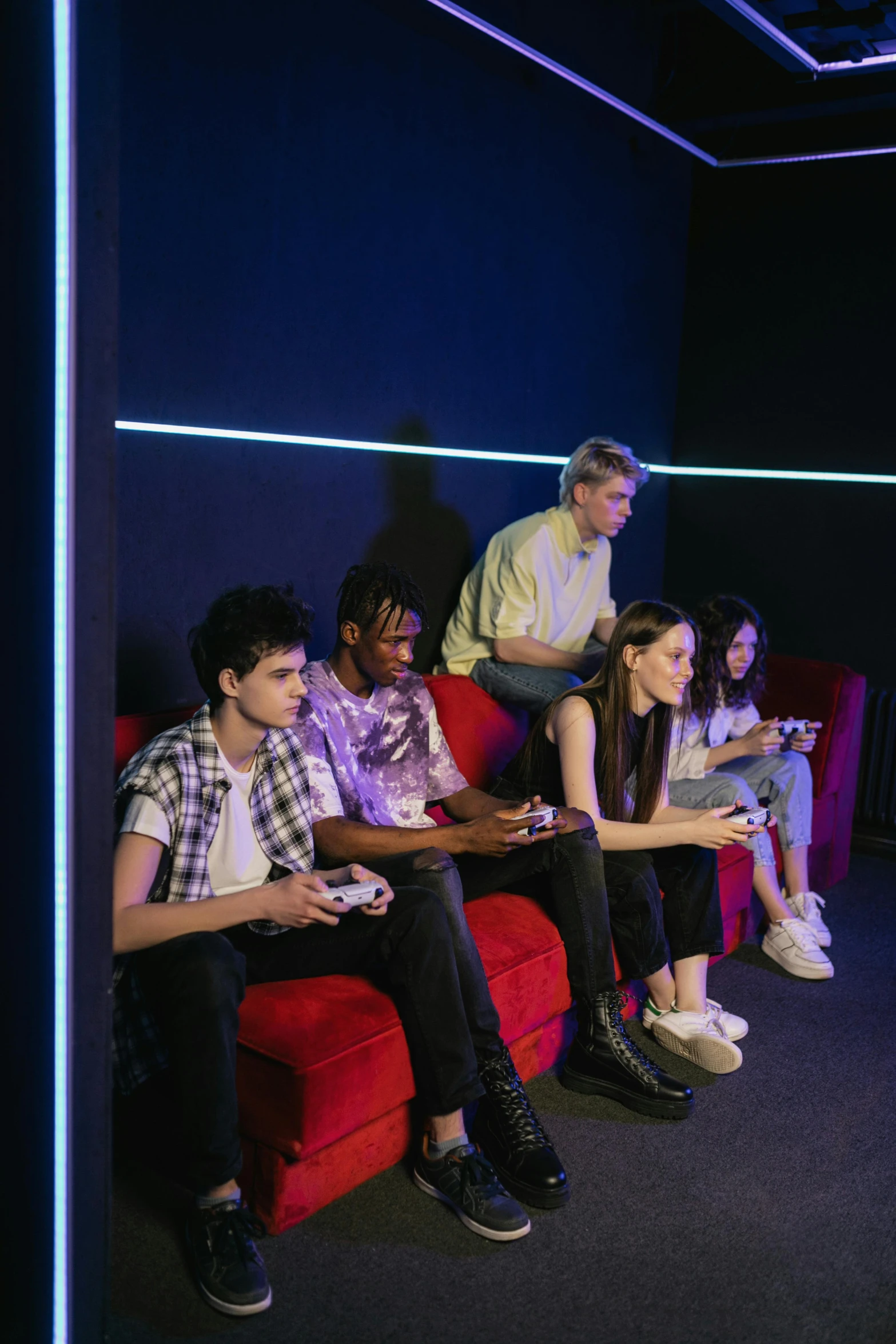 a group of people sitting on top of a red couch, pexels, gaming room in 2 0 4 0, bisexual lighting, school class, holding controller