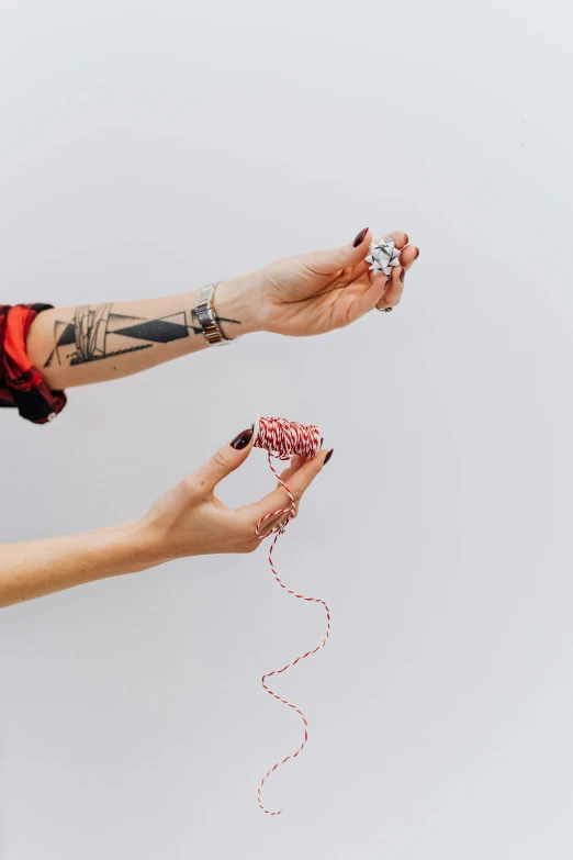 a close up of a person holding a string, a tattoo, bead and reel, red and white, product shoot, hands reaching for her