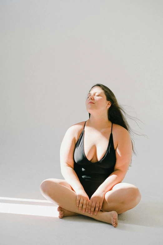 a woman in a black bodysuit sitting on the floor, unsplash, plus-sized, lotus pose, sunbathed skin, profile pic