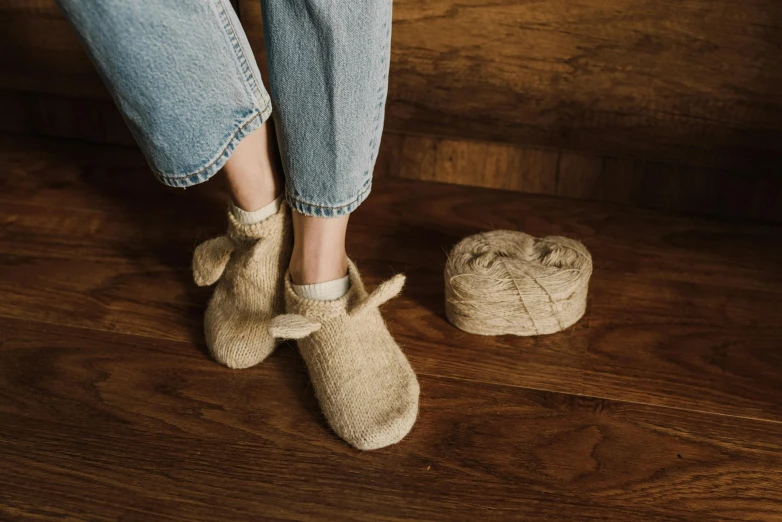 a woman standing on top of a wooden floor next to a ball of yarn, inspired by Sarah Lucas, trending on pexels, with long floppy rabbit ears, slippers, beige, burlap