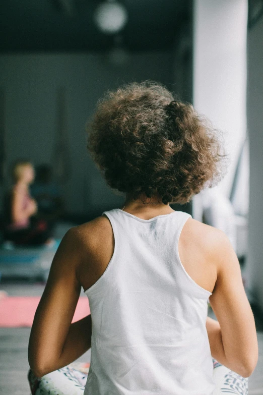 a woman sitting on a yoga mat in a gym, by Daniel Seghers, trending on pexels, happening, curly afro, from back, thumbnail, childish