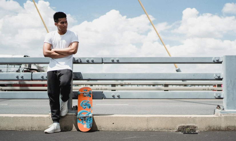 a man standing next to a skateboard on a bridge, a portrait, by Niko Henrichon, promotional image, thawan duchanee, henry ascensio, coloured photo