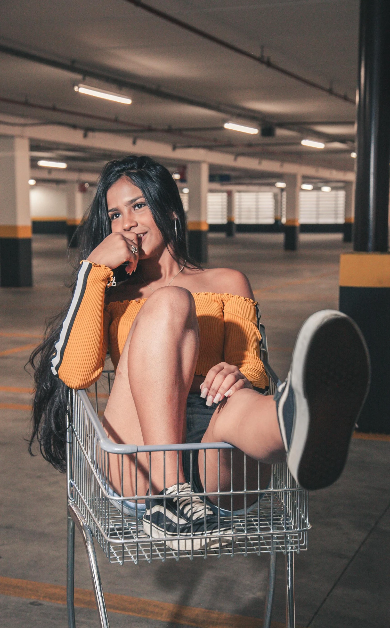 a woman sitting in a shopping cart in a parking garage, by Robbie Trevino, cute pose, high quality photo, peruvian looking, trending on imagestation