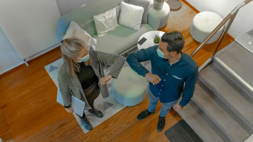 a man and a woman shaking hands in a living room, a colorized photo, by Lisa Milroy, pexels contest winner, people are wearing masks, shot from a drone, isometric 8k, looking away