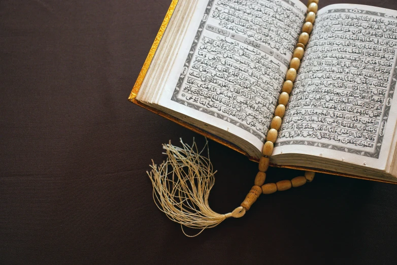 an open book sitting on top of a wooden table, hurufiyya, wearing intricate, beads, thumbnail, muslim