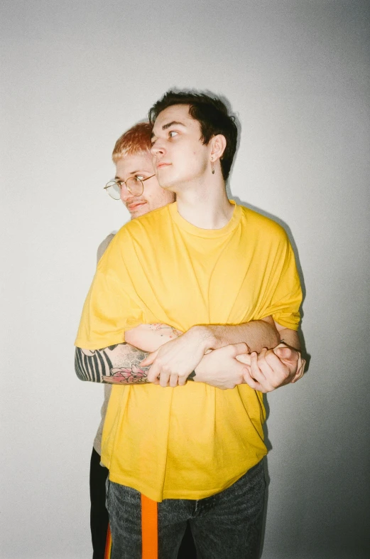 a man and a woman standing next to each other, an album cover, pexels, antipodeans, wearing a modern yellow tshirt, non binary model, hugging each other, extremely pale