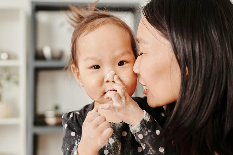 a woman holding a baby in her arms, pexels contest winner, mingei, cute bandaid on nose!!, covered in white flour, gemma chan girl portrait, manuka