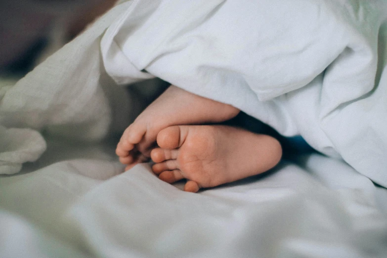 a close up of a baby's foot under a blanket, pexels contest winner, small bed not made, nursing, wearing white pajamas, legs intertwined