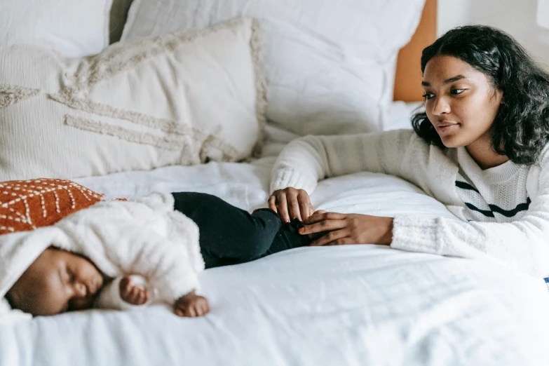 a woman laying on top of a bed next to a baby, by Carey Morris, pexels contest winner, tessa thompson, high quality details, diverse, soft and warm