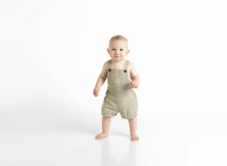 a baby standing in front of a white background, by Eero Järnefelt, professionally post - processed, overalls, hemp, taupe
