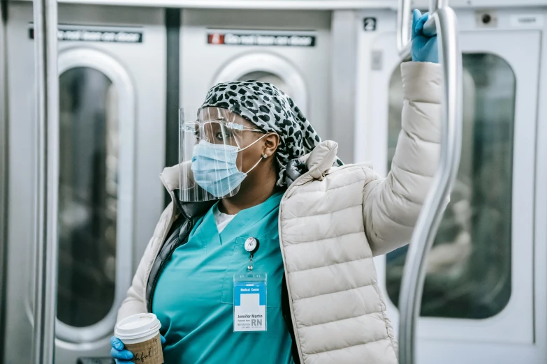 a woman wearing a face mask and holding a cup of coffee, by Meredith Dillman, pexels contest winner, happening, mta subway entrance, nurse costume, essence, on an operating table