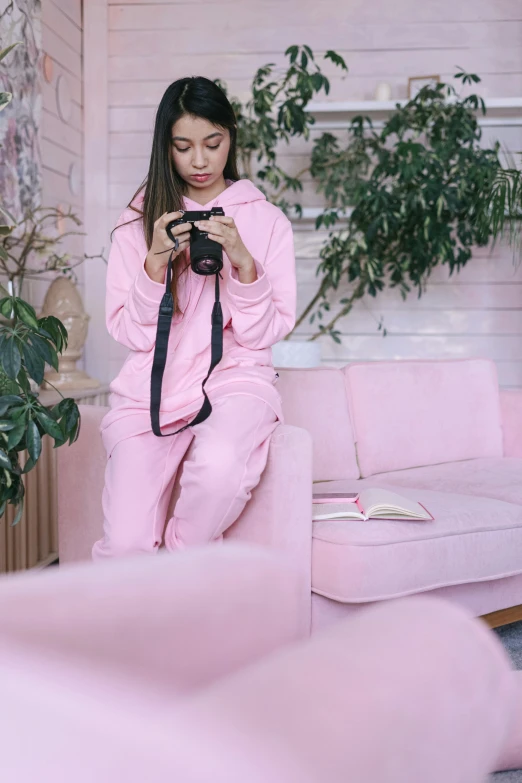 a woman sitting on a pink couch holding a camera, wearing a tracksuit, designed for cozy aesthetics!, ((pink)), college