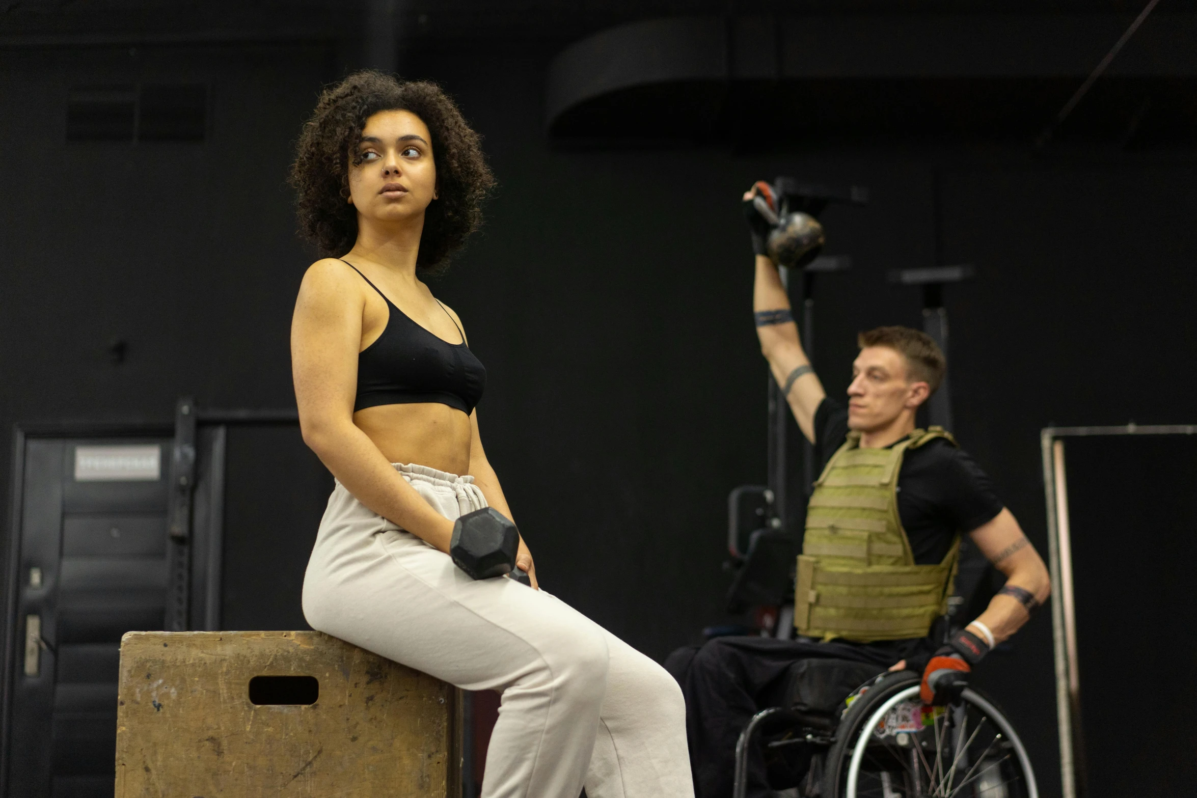 a woman sitting on top of a wooden box, charli bowater and artgeem, lifting weights, militaristic, sitting in a wheelchair