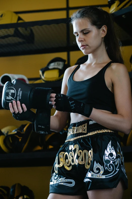a woman standing in front of a rack of boxing gloves, wearing a black cropped tank top, knee pads, shot with sony alpha, ergodox