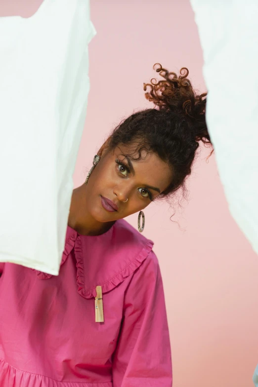 a woman holding a white shirt over her head, an album cover, pink clothes, curly messy high bun hairstyle, official store photo, ankh