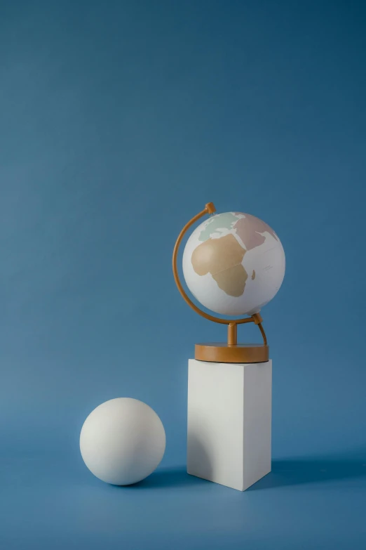 a globe sitting on top of a wooden stand next to a white ball, muted colors. ue 5, detailed product image, matte surface, playful composition