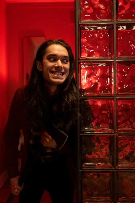 a woman standing in front of a glass block wall, an album cover, pexels contest winner, antipodeans, with red haze and a massive grin, with his long black hair, in a hotel hallway, frank dillane as puck