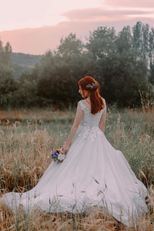 a woman in a wedding dress standing in a field, pexels contest winner, she has red hair, evening time, looking back at the camera, romantic themed