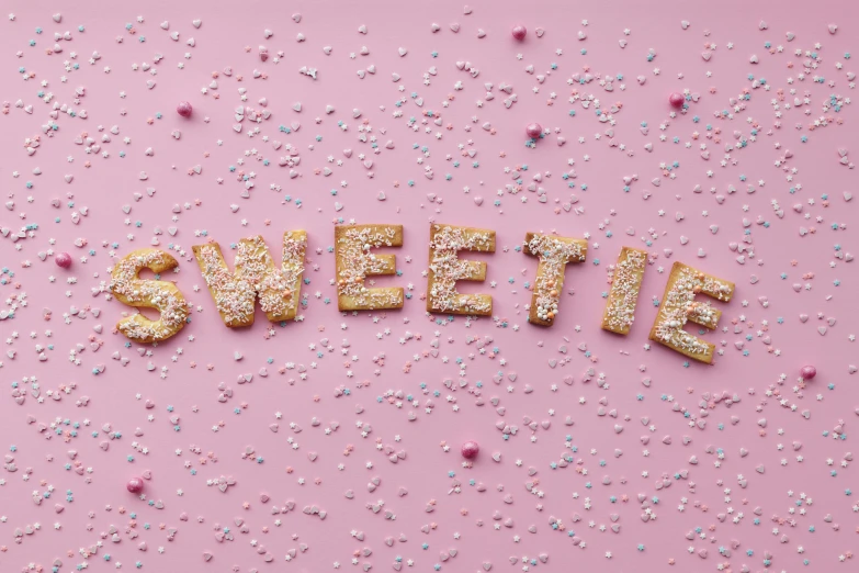the word sweetie spelled in gold letters surrounded by confetti sprinkles, by Daniel Lieske, trending on pexels, graffiti, covered with pink marzipan, 1940s food photography, cookies, 🎨🖌️