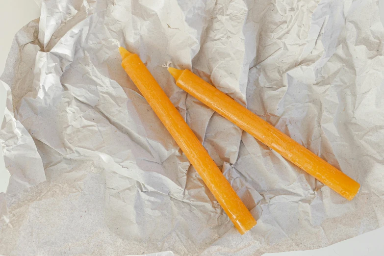 a couple of carrot sticks sitting on top of a piece of tin foil, candle wax, on parchment, slightly tanned, yellow-orange