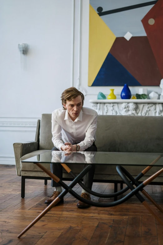 a man sitting on a couch in a living room, inspired by Oskar Lüthy, marble table, jamie campbell bower, seated at a table, 2019 trending photo