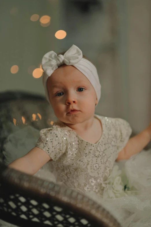 a baby girl in a white dress sitting on a chair, pexels contest winner, embellished sequined, turban, glitter gif, soft evening lighting