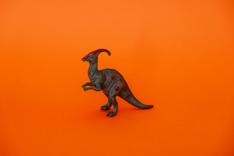 a toy dinosaur on an orange background, inspired by Adam Rex, unsplash contest winner, magic realism, red horns, bronze, asset on grey background, lecherous pose