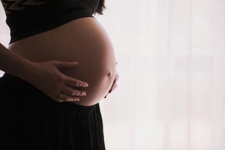 a pregnant woman standing in front of a window, closeup photograph, promo image, black, belly free