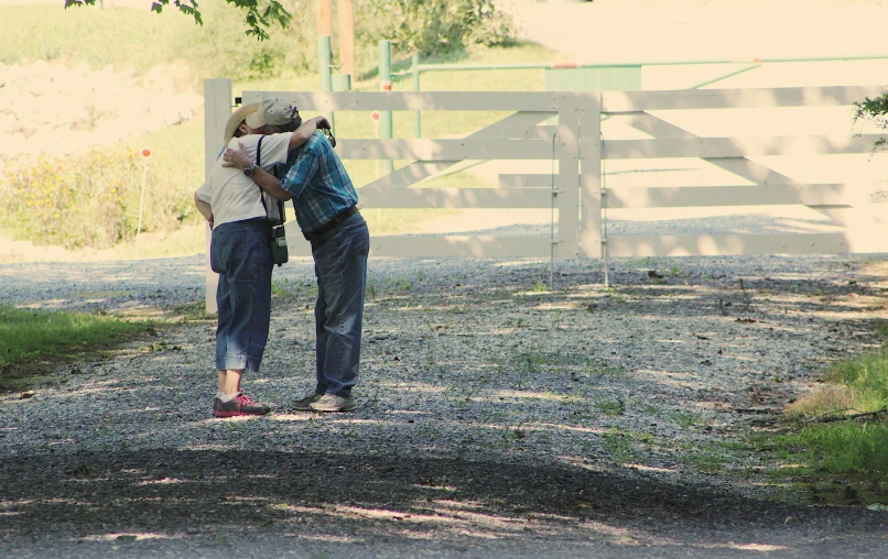 a couple of people that are standing in the dirt, by Pamela Ascherson, unsplash, photorealism, hugs, video still, on a farm, two old people