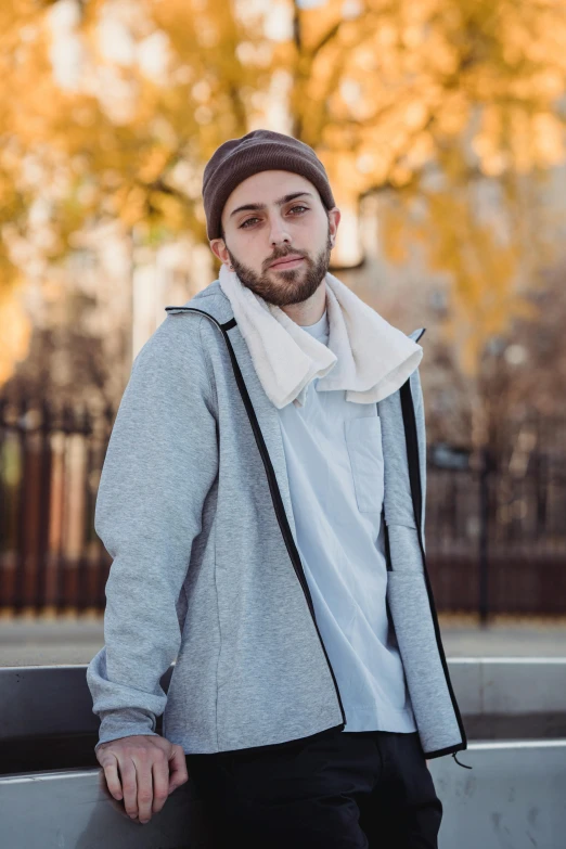 a man standing next to a wall with a skateboard, inspired by Clément Serveau, unsplash, renaissance, wearing a grey hooded sweatshirt, wearing a turtleneck and jacket, mac miller, at a park